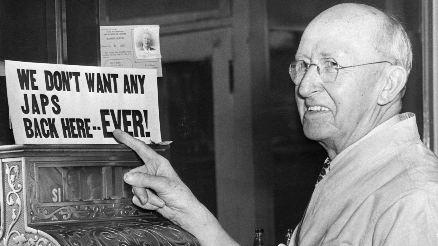 A barber points to his own anti-Japanese sign after Japanese-Americans were incarcerated during World War II